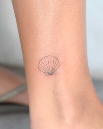 A delicate seashell tattoo on an ankle. The minimalist design features thin black lines, perfect for a summer-inspired seashell tattoo. This ankle tattoo offers a subtle, yet stylish, summer aesthetic.