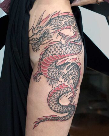 A detailed Japanese dragon tattoo in black and red ink wraps around a person's thigh. The dragon's scales are meticulously rendered, with a fierce expression on its face. This stunning dragon art is a perfect example of body art and tattoo design.