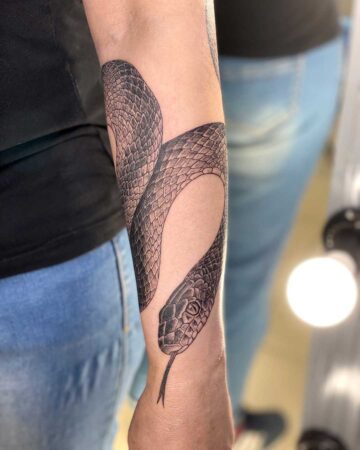 Detailed black and gray snake tattoo coiled around a forearm, featuring realistic scale detailing and a forked tongue. A striking snake tattoo design. Done by tattoo artists in our fine line tattoo studio parlour shop Canggu, Bali