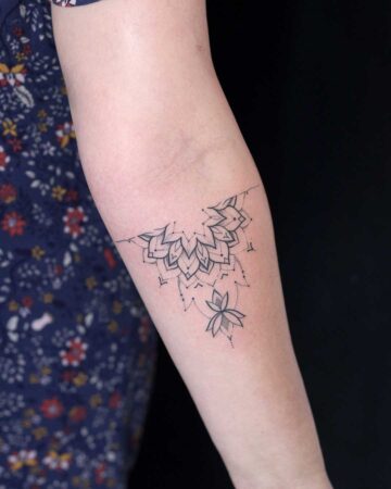 Delicate black ink mandala tattoo on a woman's forearm, featuring a detailed floral design with a lotus flower accent. This beautiful women's tattoo is a perfect example of intricate arm tattoo art. Done by tattoo artists in our fine line tattoo studio parlour shop Canggu, Bali