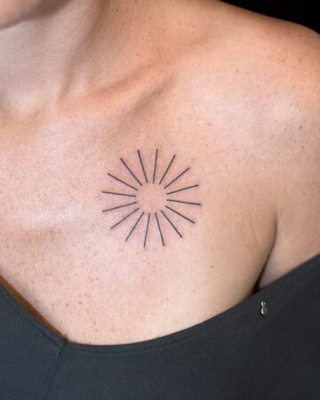 A minimalist sunburst tattoo on a woman's chest. The small, simple design features thin black lines radiating outwards from a central point, a popular choice for a small and elegant minimalist tattoo.
