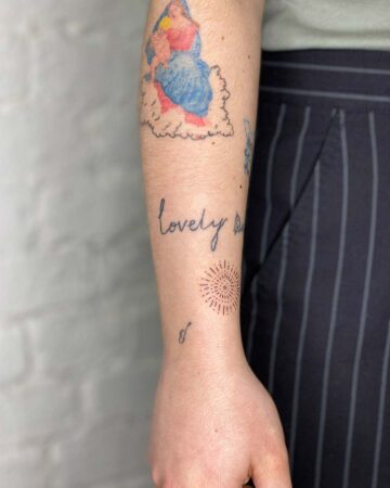 Arm with tattoos including "lovely," a sunburst design, and a small symbol. By tattoo artists in tattoo studio Canggu, Bali