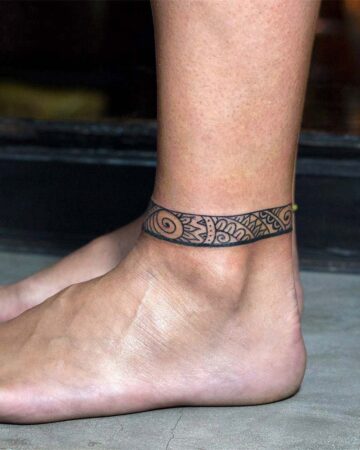 Close-up of an ankle featuring a black band tattoo design, showcasing intricate tribal patterns. This ankle tattoo is a popular tattoo design. Done by tattoo artists in our fine line tattoo studio parlour shop Canggu, Bali