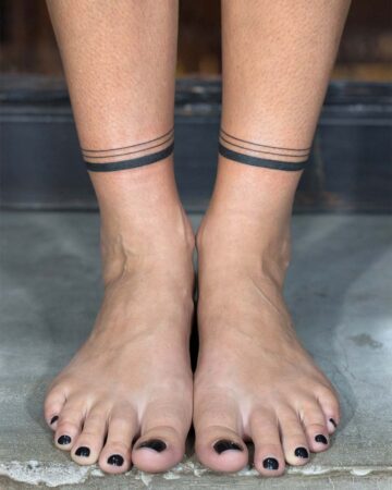 Close-up of ankles with minimalist band tattoos, perfect for summer. Featuring black nail polish, a simple and stylish ankle tattoo idea. Done by tattoo artists in our fine line tattoo studio parlour shop Canggu, Bali