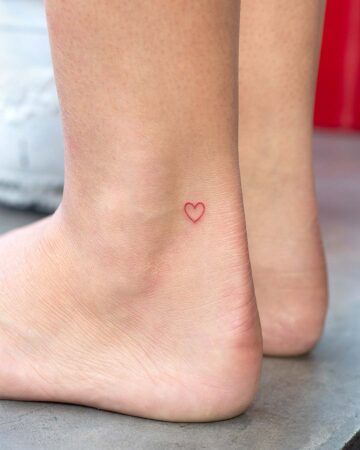 Delicate red heart tattoo on an ankle, showcasing a minimalist design. Perfect inspiration for small tattoos and ankle tattoos. Done by tattoo artists in our fine line tattoo studio parlour shop Canggu, Bali