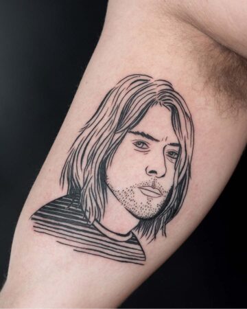 Detailed black ink tattoo of Kurt Cobain on an arm, featuring his likeness with long hair, a goatee, and a striped shirt. A tribute to the grunge music icon. Done by tattoo artists in our fine line tattoo studio parlour shop Canggu, Bali