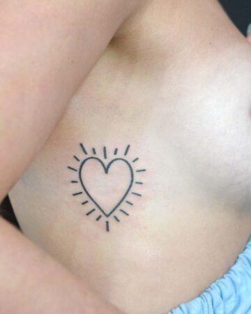 Minimalist heart tattoo on ribcage, featuring a simple heart outline with radiating lines, giving a sunburst effect. Small tattoo, ideal for first-timers. Done by tattoo artists in our fine line tattoo studio parlour shop Canggu, Bali