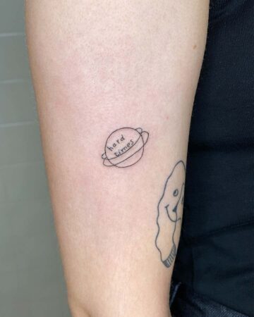 Tiny tattoo of a planet with "hard times" written on it, a visual reminder of overcoming challenges.