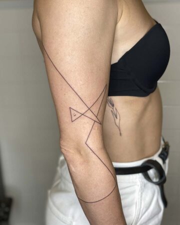 A woman's arm displays a minimalist line art tattoo featuring geometric shapes and a curved line. The tattoo, a geometric design, is inked in black and wraps around the arm, showcasing a modern minimalist tattoo style, perfect for minimalist tattoo inspiration. Done by tattoo artists in our fine line tattoo studio parlour shop Canggu, Bali