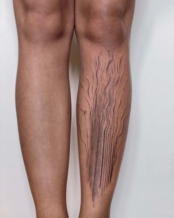 Detailed view of a leg featuring a minimalist line tattoo design. The tattoo consists of vertical and curved black lines, creating an abstract pattern along the calf. A great example of a minimalist tattoo. Done by tattoo artists in our fine line tattoo studio parlour shop Canggu, Bali