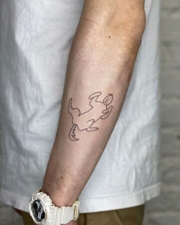 A minimalist doodle art tattoo on a forearm, featuring a whimsical figure with outstretched arms and a tail. The arm is fair-skinned, with a white G-Shock watch visible. A new tattoo, a doodle art piece. Done by tattoo artists in our fine line tattoo studio parlour shop Canggu, Bali