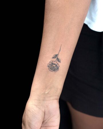 A delicate, minimalist rose tattoo on a wrist, showcasing fine line detail. The small floral tattoo features a detailed bloom and simple leaves, ideal for subtle rose tattoo designs. Done by tattoo artists in our fine line tattoo studio parlour shop Canggu, Bali