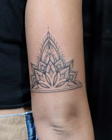 Intricate mandala tattoo design on an arm, featuring a symmetrical pattern of petals and geometric shapes. The black ink tattoo is positioned above the elbow, with a delicate line border. Done by tattoo artists in our fine line tattoo studio parlour shop Canggu, Bali