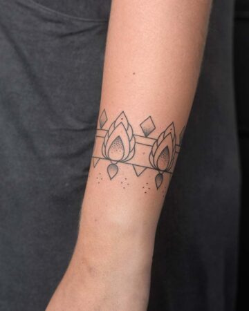 Close-up of an arm with a minimalist floral tattoo design. The tattoo features stylized lotus-like flowers, geometric shapes, and dotted accents, forming a band around the arm. This arm tattoo is a great source of minimalist tattoo inspiration. Done by tattoo artists in our fine line tattoo studio parlour shop Canggu, Bali
