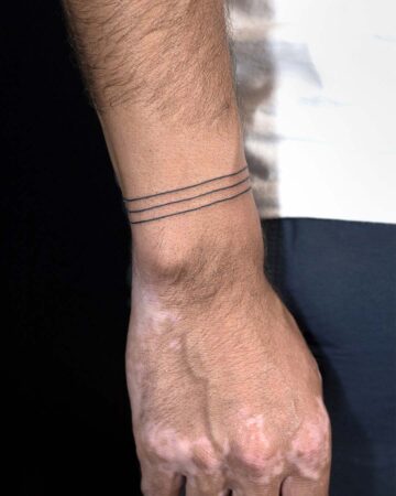 Close-up of a wrist with a minimalist line tattoo. Three thin, black lines encircle the wrist, a simple and elegant design. The skin tone is fair, with some areas of discoloration. Done by tattoo artists in our fine line tattoo studio parlour shop Canggu, Bali