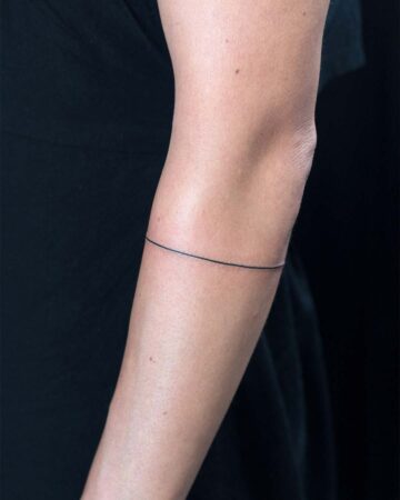 A thin, black line tattoo encircles a person's forearm. The simple design offers a minimalist aesthetic, perfect for those seeking a simple tattoo. This arm tattoo is a popular minimalist tattoo choice. Done by tattoo artists in our fine line tattoo studio parlour shop Canggu, Bali