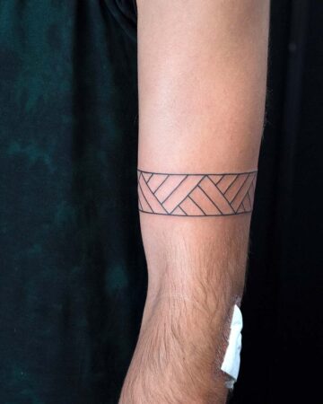 Close-up of a forearm featuring a geometric armband tattoo with a minimalist design. The black ink creates a repeating pattern around the arm, showcasing a modern tattoo design. Done by tattoo artists in our fine line tattoo studio parlour shop Canggu, Bali