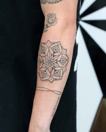 Detailed mandala tattoo on an arm, featuring intricate geometric patterns and a central star design. Below, a delicate dotted line band tattoo and script that reads "poušť k moři". A small rose tattoo is also visible. Done by tattoo artists in our fine line tattoo studio parlour shop Canggu, Bali