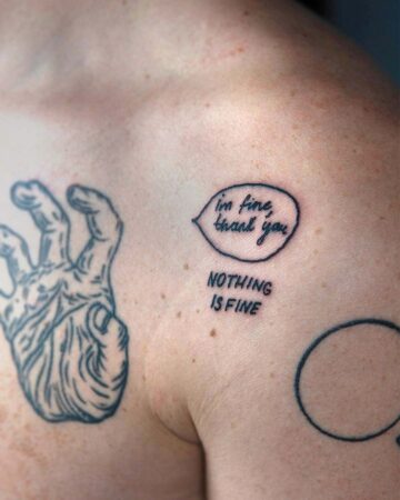 A person's shoulder and upper chest displaying multiple tattoos. One tattoo is a hand with fingers in a peace sign. A speech bubble tattoo says "I'm fine, thank you" with the words "Nothing is fine" underneath. Another tattoo is a simple circle. Done by tattoo artists in our fine line tattoo studio parlour shop Canggu, Bali