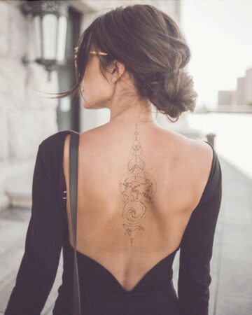 Woman with dark hair in a bun, wearing a black, low-back dress, showing off a minimalist tattoo design on her back. The tattoo features geometric shapes, a world map, and a whale, showcasing tattoo designs and fashion trends. Done by tattoo artists in our fine line tattoo studio parlour shop Canggu, Bali