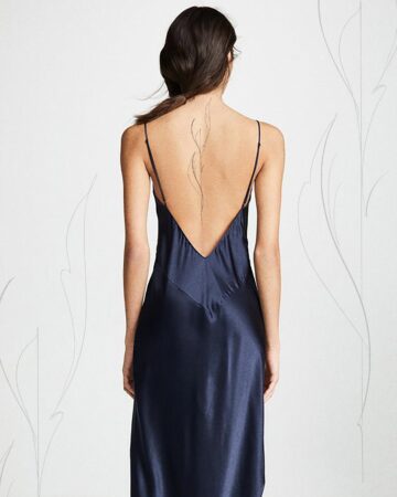 Woman with dark hair in a navy blue slip dress, showcasing a delicate, fine-line back tattoo. The tattoo design is a minimalist, organic shape, perfect for minimalist tattoos. Done by tattoo artists in our fine line tattoo studio parlour shop Canggu, Bali