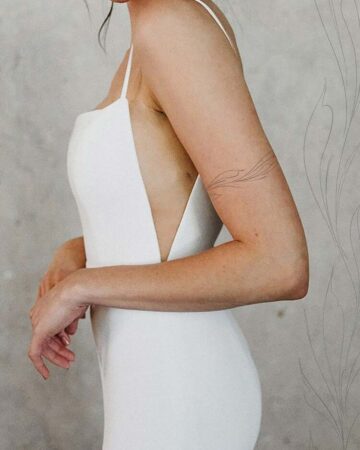 A bride in a simple wedding dress with a minimalist design, featuring a low back and spaghetti straps. She has a delicate arm tattoo. Perfect for a modern bride. Done by tattoo artists in our fine line tattoo studio parlour shop Canggu, Bali