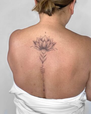 Delicate lotus flower tattoo on a woman's back. The minimalist design features a detailed lotus blossom, a stylized stem, and a line of symbols down the spine. A beautiful example of a spine tattoo. Done by tattoo artists in our fine line tattoo studio parlour shop Canggu, Bali