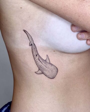 A minimalist whale shark tattoo on a woman's ribcage, showcasing the detailed dotwork design. The tattoo is in black ink and is a popular choice for a rib tattoo. Done by tattoo artists in our fine line tattoo studio parlour shop Canggu, Bali