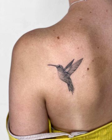 Delicate hummingbird tattoo on a shoulder, featuring detailed shading and outstretched wings, a perfect example of a small bird tattoo design. Done by tattoo artists in our fine line tattoo studio parlour shop Canggu, Bali
