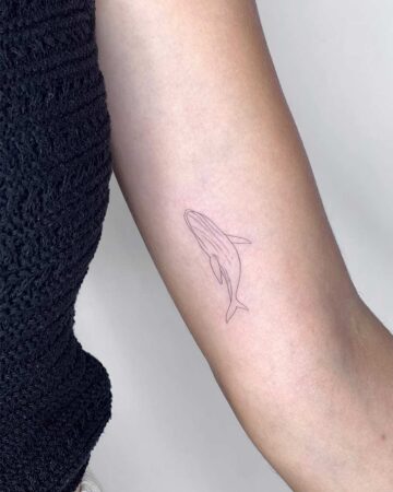 Delicate minimalist whale tattoo on arm. The small tattoo features fine lines, with the whale angled slightly downward. A great small tattoo idea. Done by tattoo artists in our fine line tattoo studio parlour shop Canggu, Bali