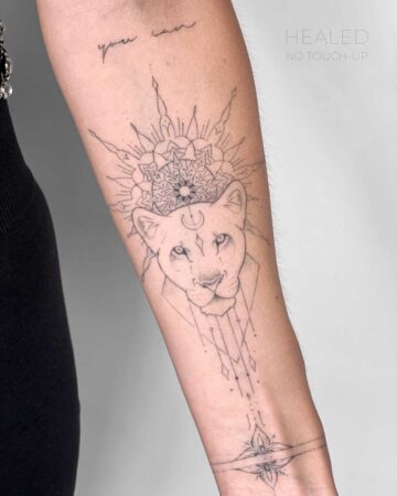 Delicate fine line lion tattoo on an arm, incorporating a mandala design above the lion's head. The tattoo features geometric details and a floral bracelet design at the wrist. Text reads "Healed, No Touch-Up. Done by tattoo artists in our fine line tattoo studio parlour shop Canggu, Bali