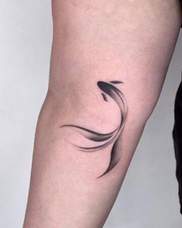 Minimalist black fish tattoo on an arm, featuring flowing lines and shading. A small, elegant design, perfect for tattoo inspiration. Done by tattoo artists in our fine line tattoo studio parlour shop Canggu, Bali
