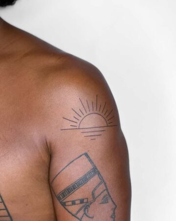 Minimalist sun tattoo on a shoulder, featuring a simple design of a half-circle sun with radiating lines above a horizon line; perfect for summer tattoos. Done by tattoo artists in our fine line tattoo studio parlour shop Canggu, Bali