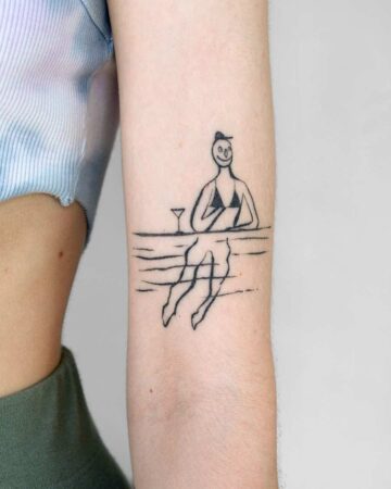 Minimalist tattoo of a smiling person in a bikini, enjoying a cocktail at a beach bar, with their legs submerged in water. Summer tattoo inspiration. Done by tattoo artists in our fine line tattoo studio parlour shop Canggu, Bali