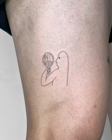A minimalist tattoo on a thigh depicts a figure holding a magnifying glass that reads "antibody." The fine line tattoo style emphasizes simplicity and concept, a popular trend in body art. Done by tattoo artists in our fine line tattoo studio parlour shop Canggu, Bali