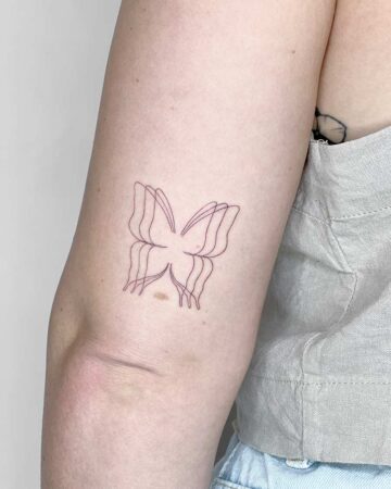 A delicate minimalist butterfly tattoo on a person's arm, featuring a fine line design. The butterfly design is slightly blurred, creating a sense of movement. This minimalist tattoo would be a great addition to any collection. Done by tattoo artists in our fine line tattoo studio parlour shop Canggu, Bali