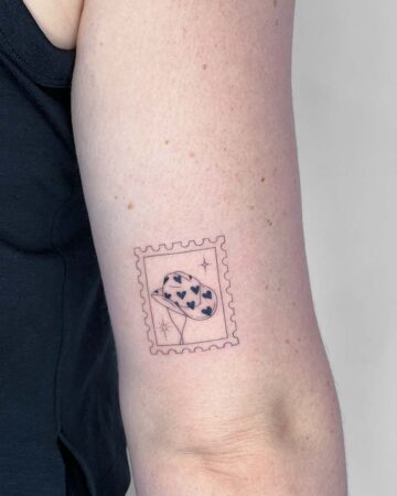 Minimalist stamp tattoo on an arm, featuring a cowboy hat with heart-shaped details. The tattoo is outlined in black ink, inside a classic stamp border, perfect for unique tattoo inspiration. Done by tattoo artists in our fine line tattoo studio parlour shop Canggu, Bali