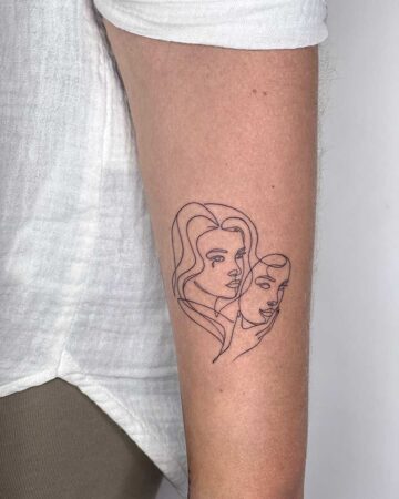 A minimalist tattoo on an arm depicts two faces in a continuous line. One face, a woman with a tear, and the other, a mask, symbolizing the journey of self-discovery and mental health. Done by tattoo artists in our fine line tattoo studio parlour shop Canggu, Bali