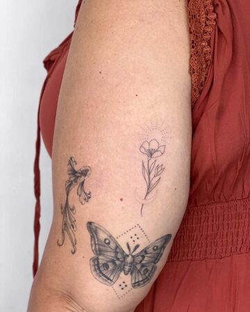 Close-up of a woman's arm featuring four delicate black ink tattoos: a butterfly with detailed wing patterns, a stylized flower, a flowing ornamental design, and a minimalist floral tattoo design. The tattoos are placed on the arm against the backdrop of a rust-colored dress, showcasing nature-inspired tattoo art. Done by tattoo artists in our fine line tattoo studio parlour shop Canggu, Bali