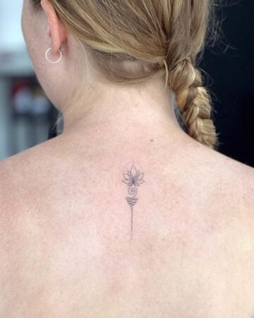 Delicate minimalist lotus flower tattoo on a woman's back, featuring the Unalome symbol. The fine-line design suggests a spiritual tattoo, with the lotus and Unalome representing enlightenment. Done by tattoo artists in our fine line tattoo studio parlour shop Canggu, Bali