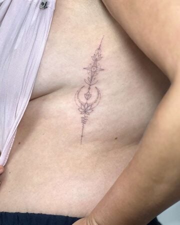 A delicate, minimalist rib tattoo on a woman's side, featuring a vertical design with a lotus flower, crescent moon, and starburst. The fine-line tattoo is a beautiful example of a small tattoo. Done by tattoo artists in our fine line tattoo studio parlour shop Canggu, Bali