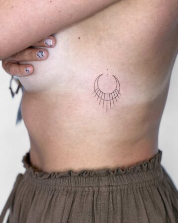 A woman's side profile reveals a delicate minimalist tattoo on her ribcage. The fine line design features a crescent moon shape with downward lines, a subtle and stylish example of a minimalist tattoo. Done by tattoo artists in our fine line tattoo studio parlour shop Canggu, Bali