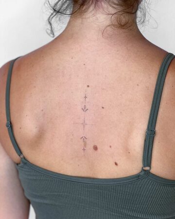 Delicate minimalist tattoo on a woman's back. A vertical line of small, intricate designs, including leaves and stars, runs down the spine, offering inspiration for small, delicate tattoos. Done by tattoo artists in our fine line tattoo studio parlour shop Canggu, Bali