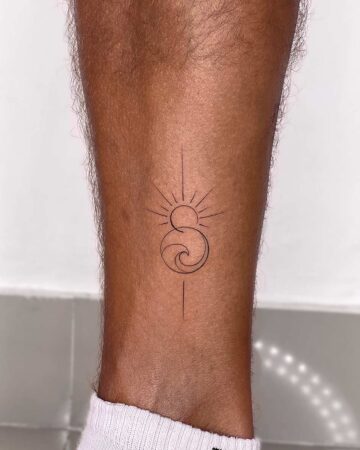 A minimalist sun and wave tattoo on a leg. The delicate black ink design features a sun with radiating lines above a stylized wave, and a vertical line below, ideal for a small ankle tattoo. Done by tattoo artists in our fine line tattoo studio parlour shop Canggu, Bali