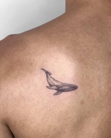 Delicate whale tattoo on the upper back, a minimalist design perfect for ocean lovers. This small tattoo features fine lines and shading, ideal for those seeking a subtle yet meaningful body art piece. Done by tattoo artists in our fine line tattoo studio parlour shop Canggu, Bali