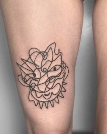 Abstract line art tattoo of a face on a thigh. The design features a chaotic, scribbled style with eyes, a mouth, and a spiky collar. A unique example of line art and thigh tattoo work. done by artists in our fine line tattoo studio Canguu Bali