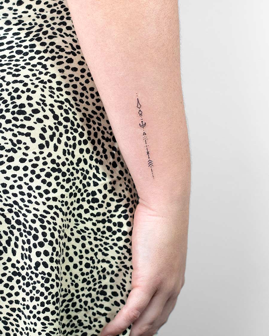 Close-up of a woman's arm showcasing a delicate, minimalist tattoo. The fine line tattoo features a series of geometric shapes and symbols, a popular style for small tattoos. Done by tattoo artists in our fine line tattoo studio parlour shop Canggu, Bali