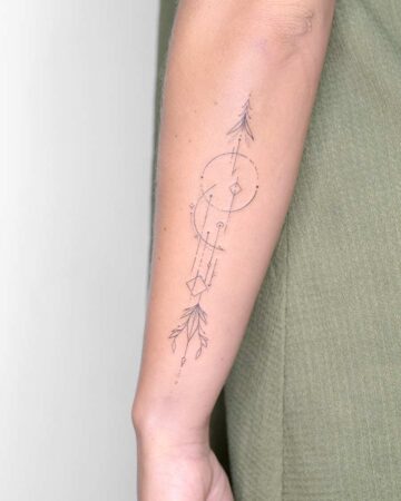 Delicate minimalist arrow tattoo on a forearm, featuring fine lines and geometric shapes, including a circle, diamond, and stylized leaves. A beautiful example of a geometric tattoo. Done by tattoo artists in our fine line tattoo studio parlour shop Canggu, Bali