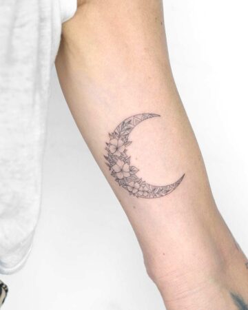 Delicate crescent moon tattoo on a woman's arm, filled with intricate floral designs and geometric patterns. A beautiful example of a feminine tattoo, combining the popular moon tattoo and floral tattoo styles. Done by tattoo artists in our fine line tattoo studio parlour shop Canggu, Bali