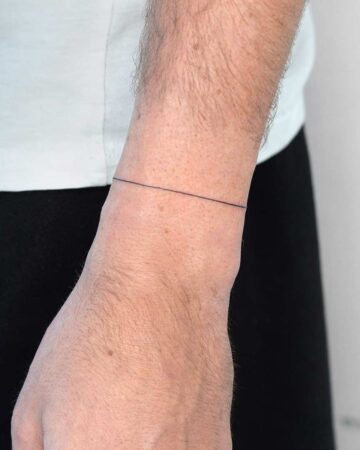 Close-up of a man's wrist featuring a single, thin black line tattoo. This minimalist tattoo design is a simple and elegant example of fine line tattoos. The tattoo is placed on the wrist, a popular location for minimalist tattoos. Done by tattoo artists in our fine line tattoo studio parlour shop Canggu, Bali
